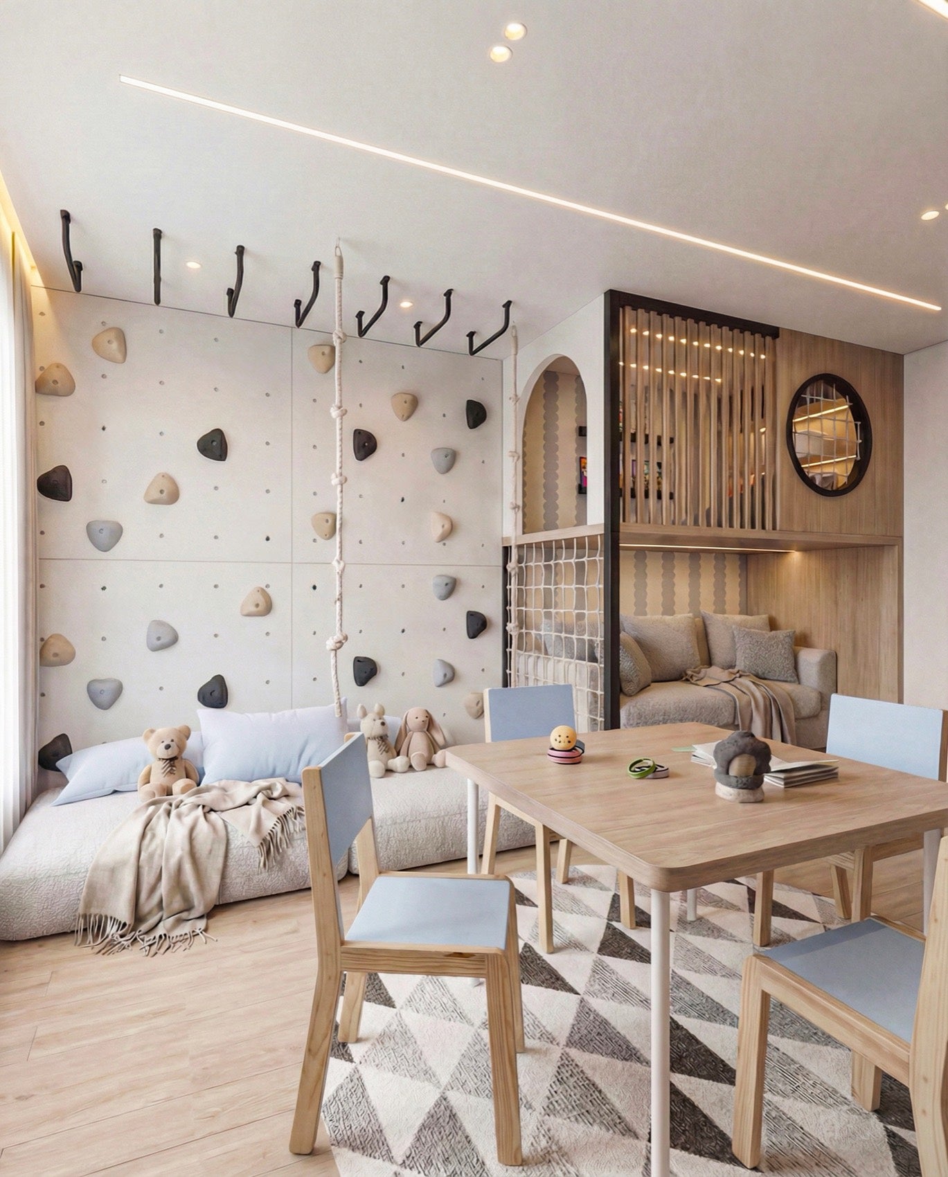 A children's room Henrique designed: a climbing wall of pale panels with grey and black holds along one side, a knotted rope hanging from ceiling hooks, a low daybed with cushions and soft toys at its foot, and a loft to the right behind a slatted screen with a round black framed window and a reading sofa tucked underneath.