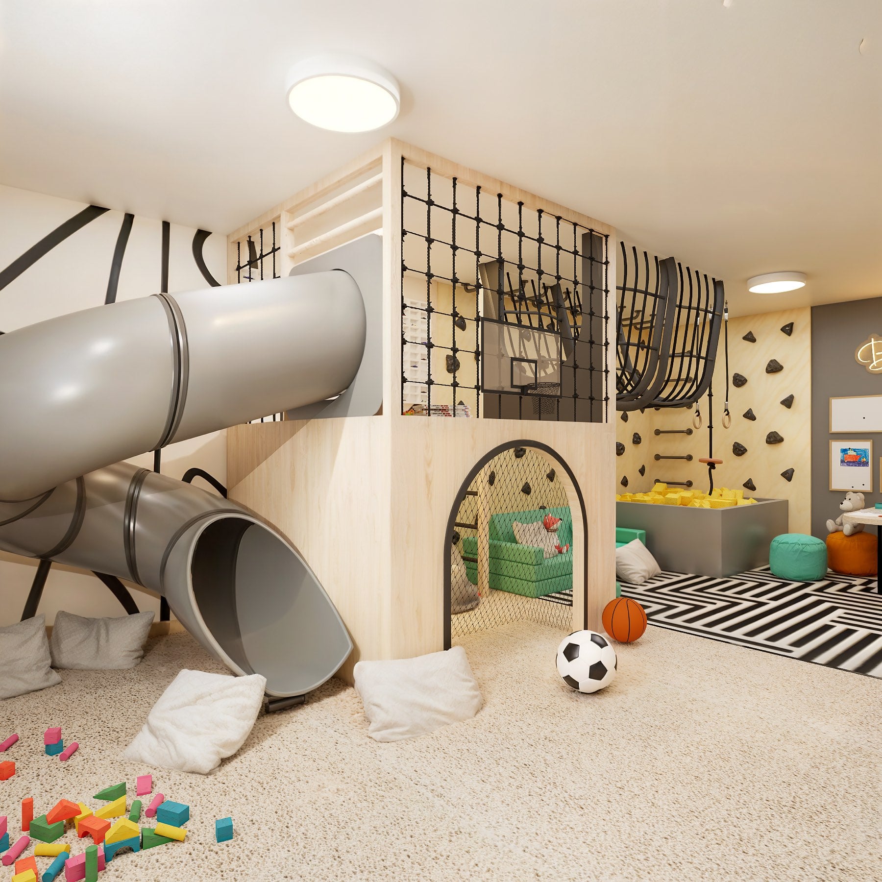 A Funte playroom: a grey tube slide running down from a plywood mezzanine, a rope climbing net and a basketball hoop above an arched den with a green sofa inside it, and along the far wall a climbing wall with holds, gym rings and a yellow foam pit.